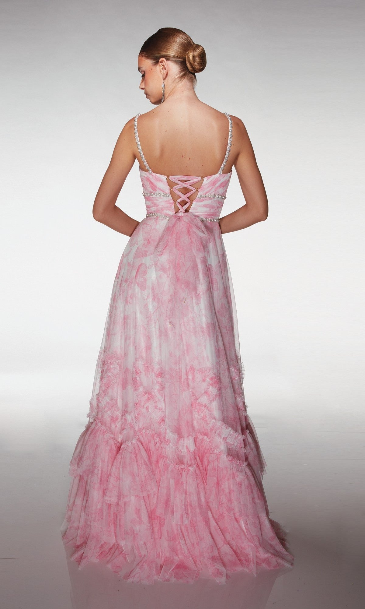 A woman stands facing away against a plain background, wearing the floor-length Alyce 62063 long formal dress in pink with a lace-up back detail.